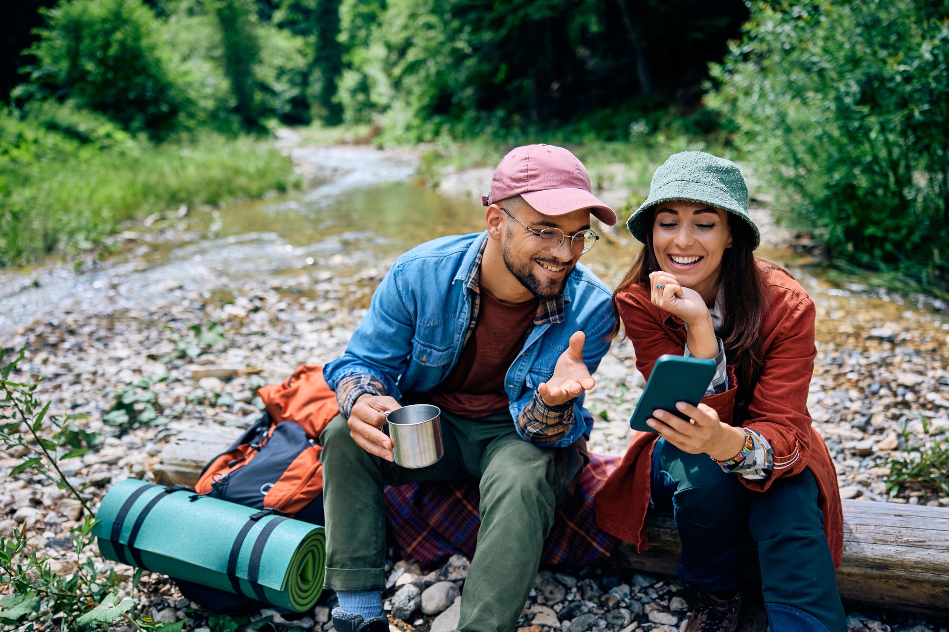 Happy couple using mobile phone while camping in the woods.