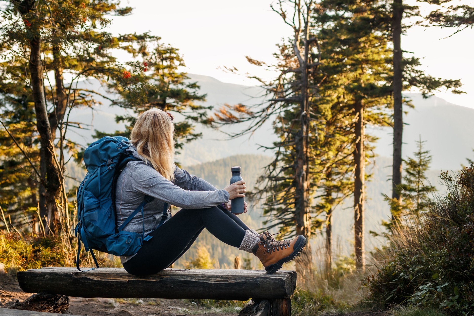 Woman with backpack and thermos sitting on bench in forest